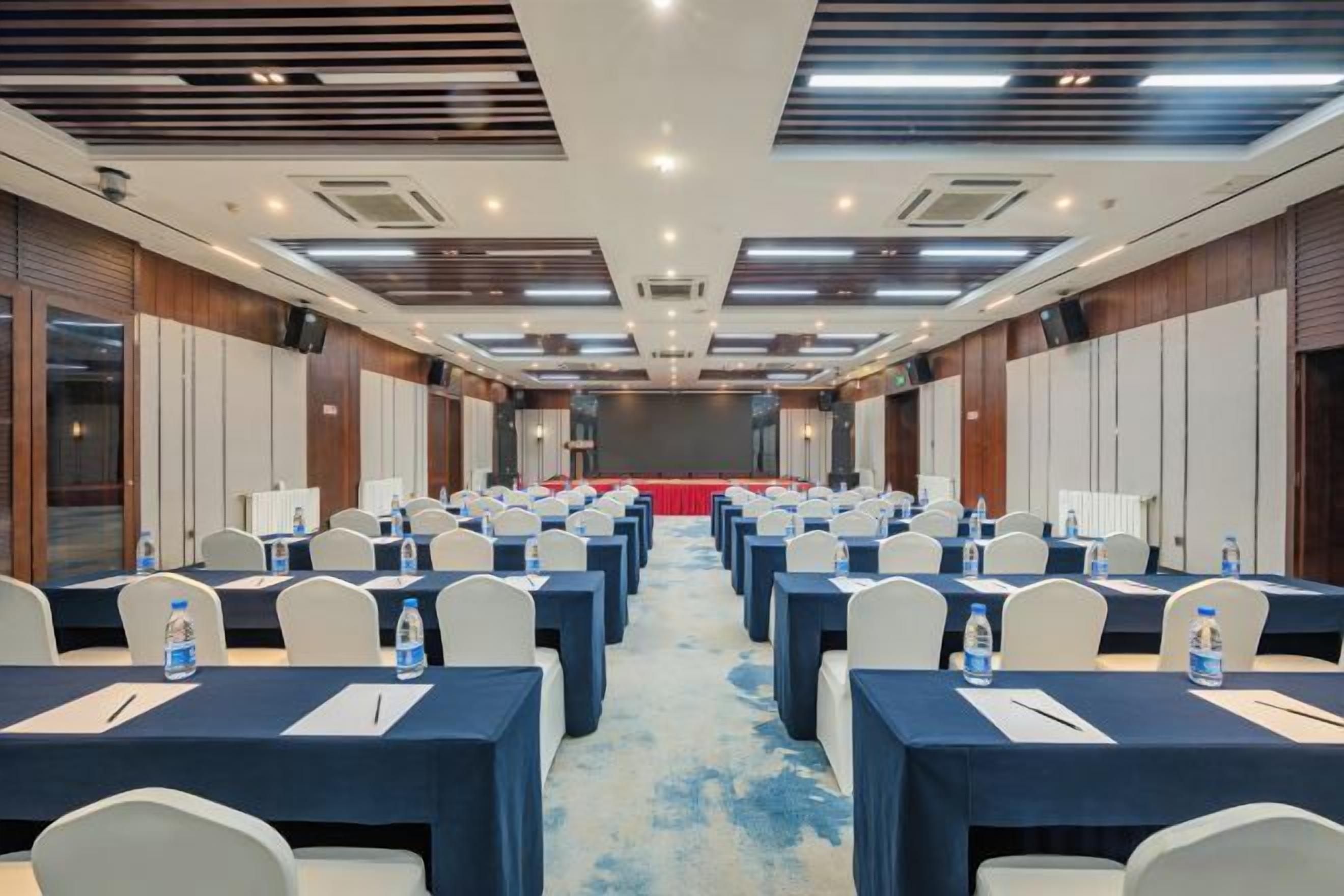 Un salón de conferencias con filas de mesas y sillas, equipado con botellas de agua y cuadernos.