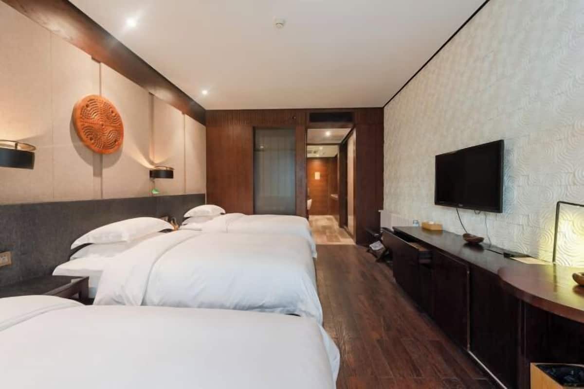 Une chambre d’hôtel avec trois lits, un téléviseur, un bureau en bois et un mur décoré d’un motif.