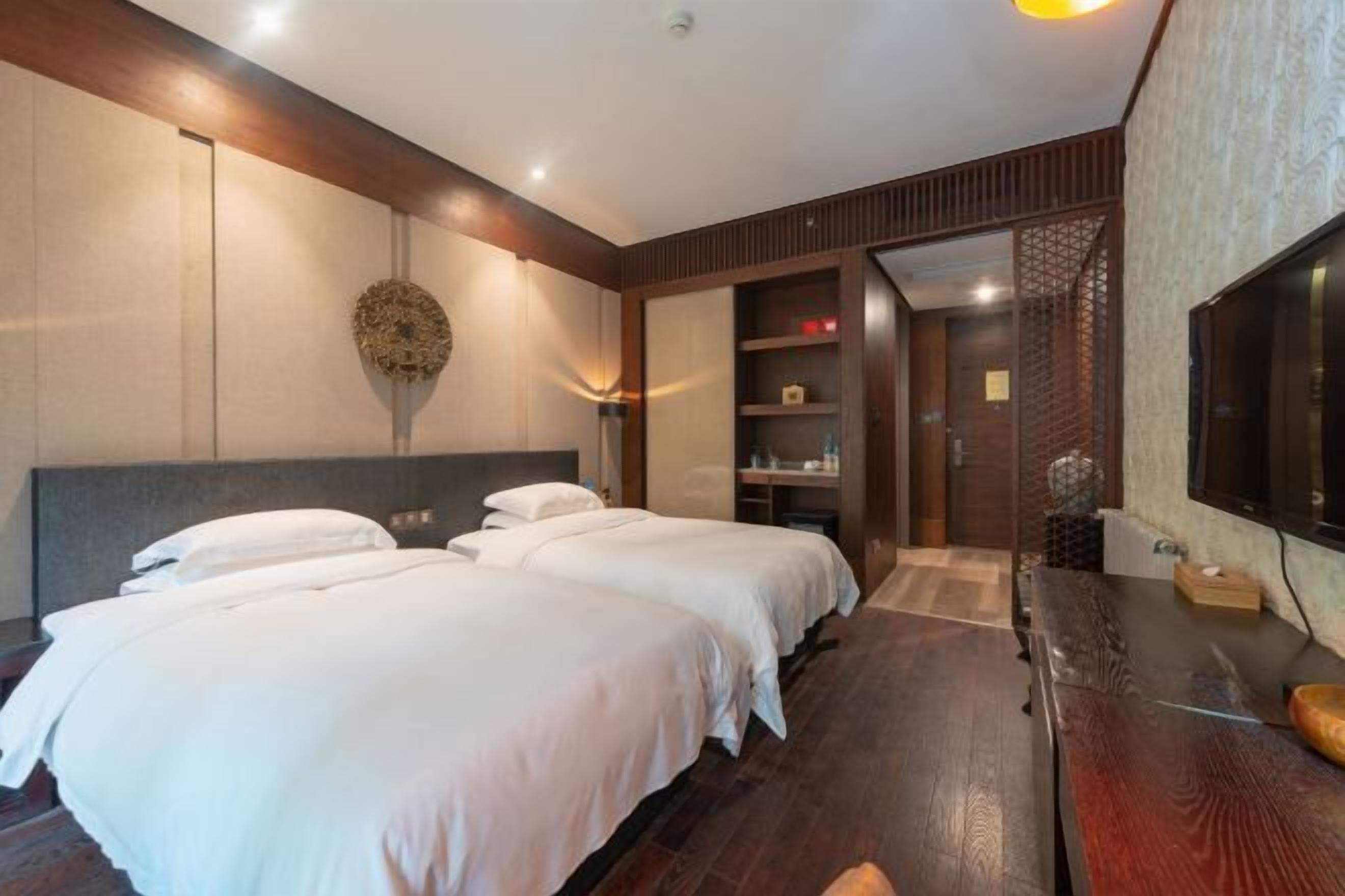 A hotel room with two beds, a TV, a wooden bench, and a decorative wall piece.