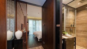 A hotel room with a wooden floor, a bed with a white bedspread, a small table with toiletries, and a decorative partition with geometric patterns. - Nanchang Qinyuan Villa (Nanchang)