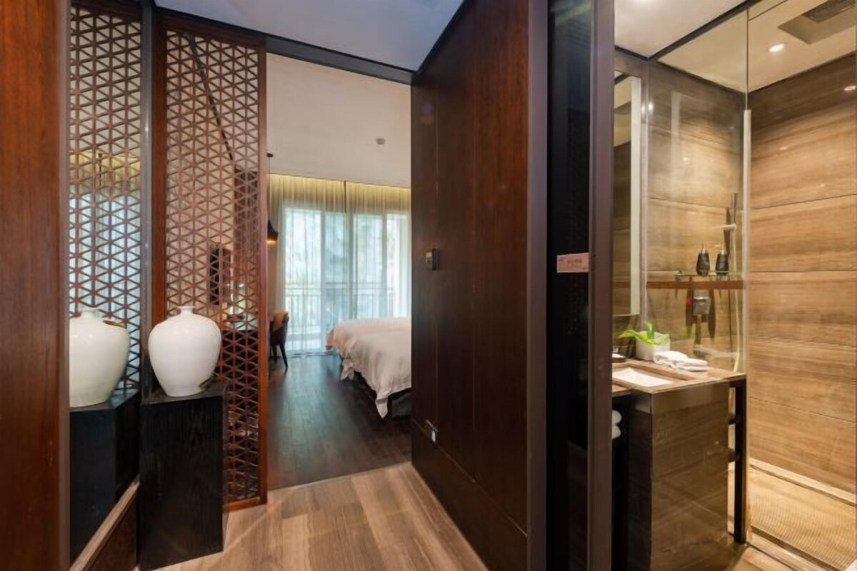 A hotel room with a wooden floor, a bed with a white bedspread, a small table with toiletries, and a decorative partition with geometric patterns.