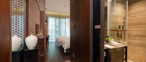 A hotel room with a wooden floor, a bed with a white bedspread, a small table with toiletries, and a decorative partition with geometric patterns.