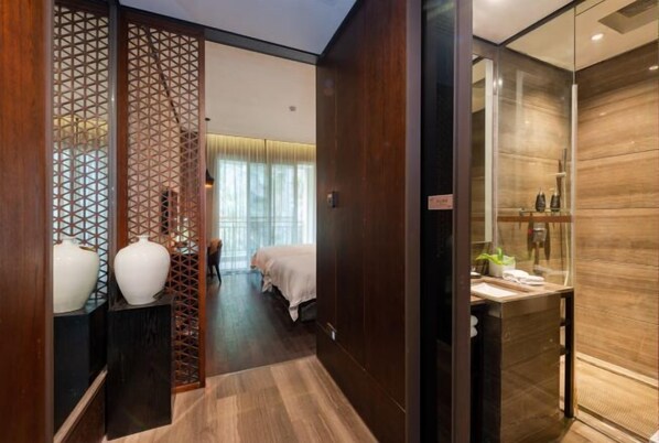 A hotel room with a wooden floor, a bed with a white bedspread, a small table with toiletries, and a decorative partition with geometric patterns. - Nanchang Qinyuan Villa (Nanchang)