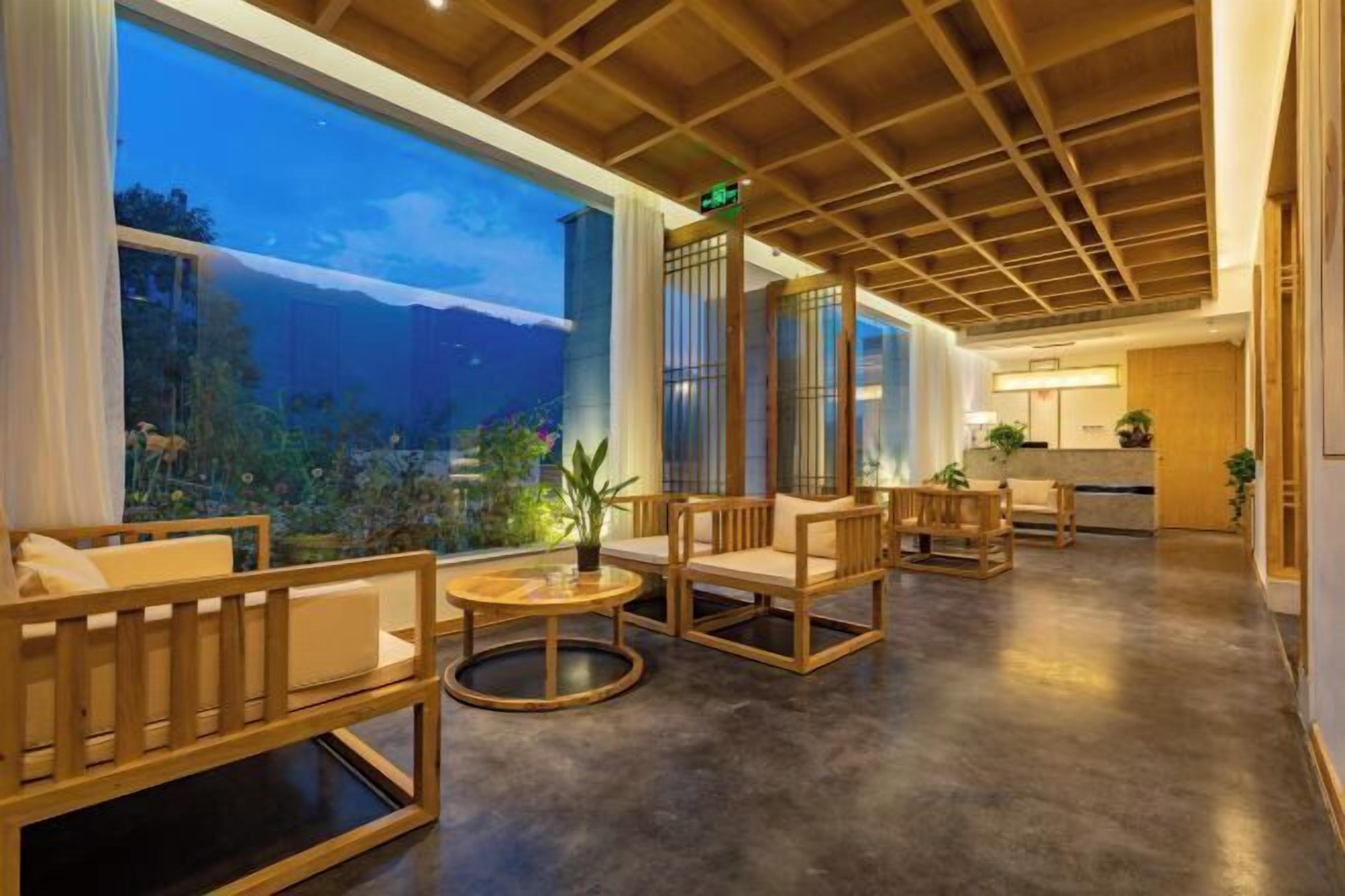 A spacious lobby with wooden furniture, large windows, and a view of a mountainous landscape.