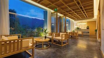 A spacious lobby with wooden furniture, large windows, and a view of a mountainous landscape.