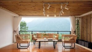 A room with a wooden floor, a sofa, two armchairs, a coffee table, and a view of mountains through a large window. - Zhangjiajie Wulingyuan Bamboo Holiday Homestay (Zhangjiajie)