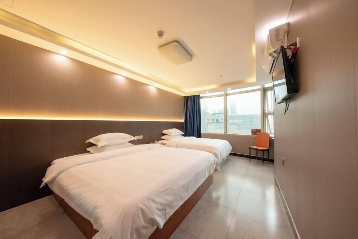 A hotel room with a large bed, a TV mounted on the wall, and a view of the city through the window.