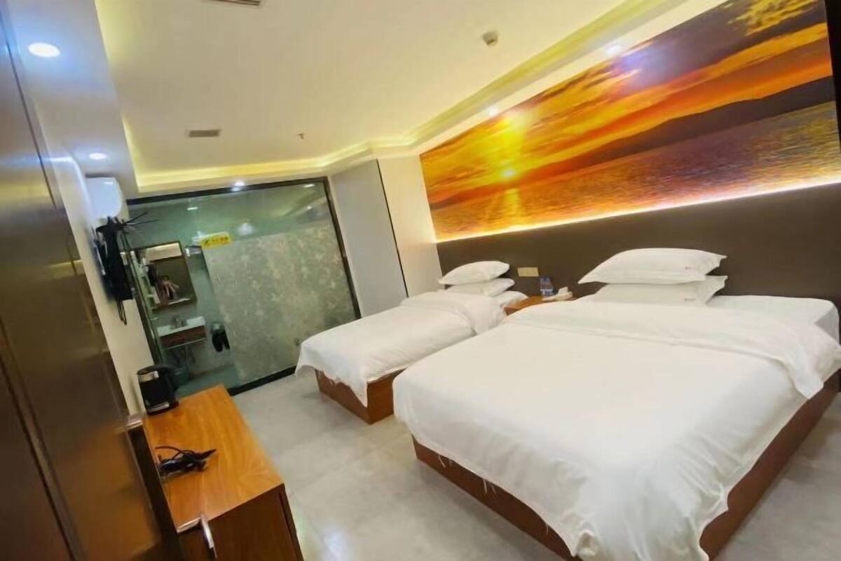 A hotel room with two beds, a desk, a mirror, and a large abstract wall mural.