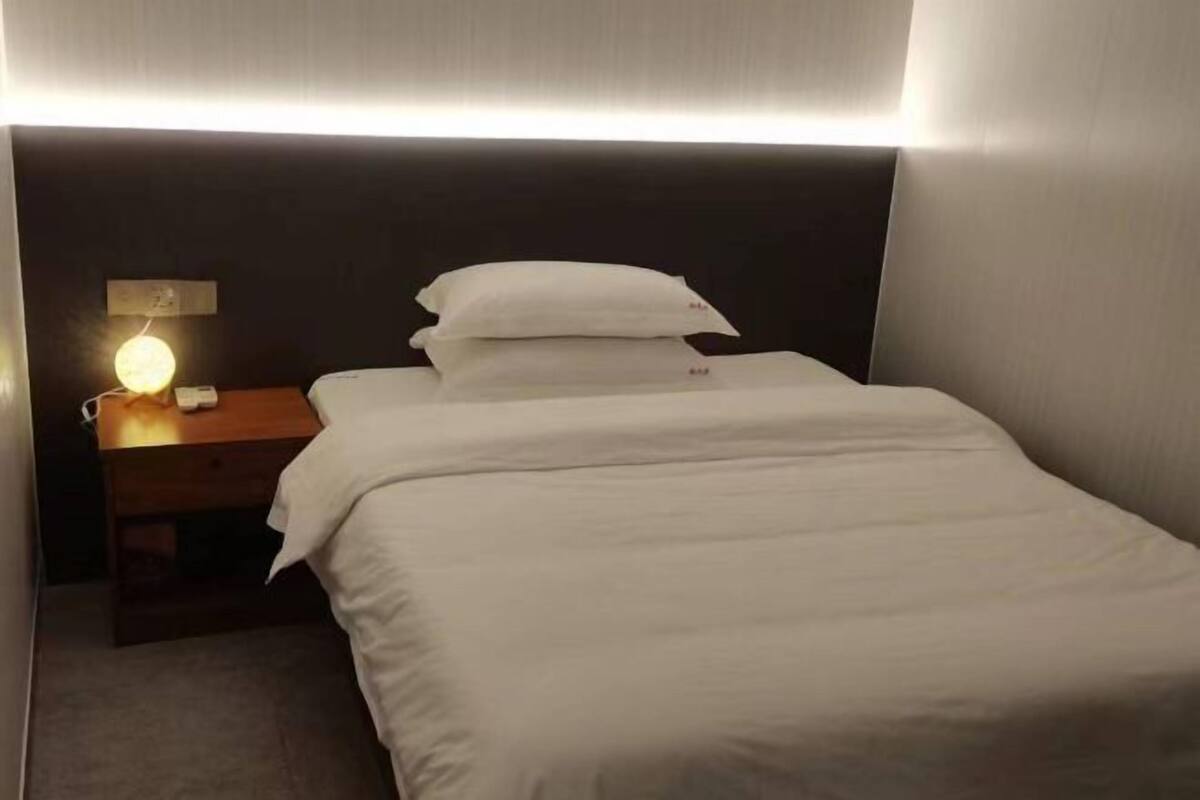 A neatly made bed with white bedding, a wooden nightstand with a lamp, and a dark headboard.