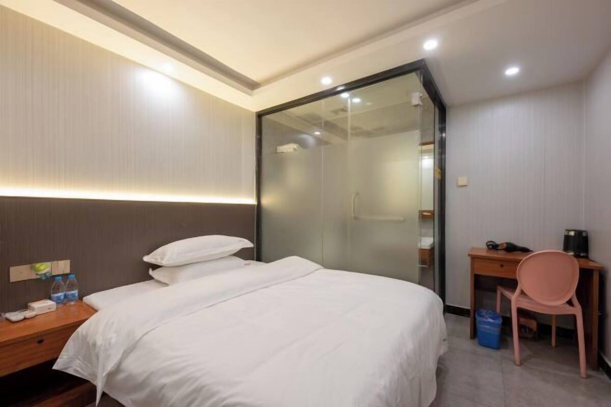 A hotel room with a bed, a desk, a chair, and a glass shower enclosure.