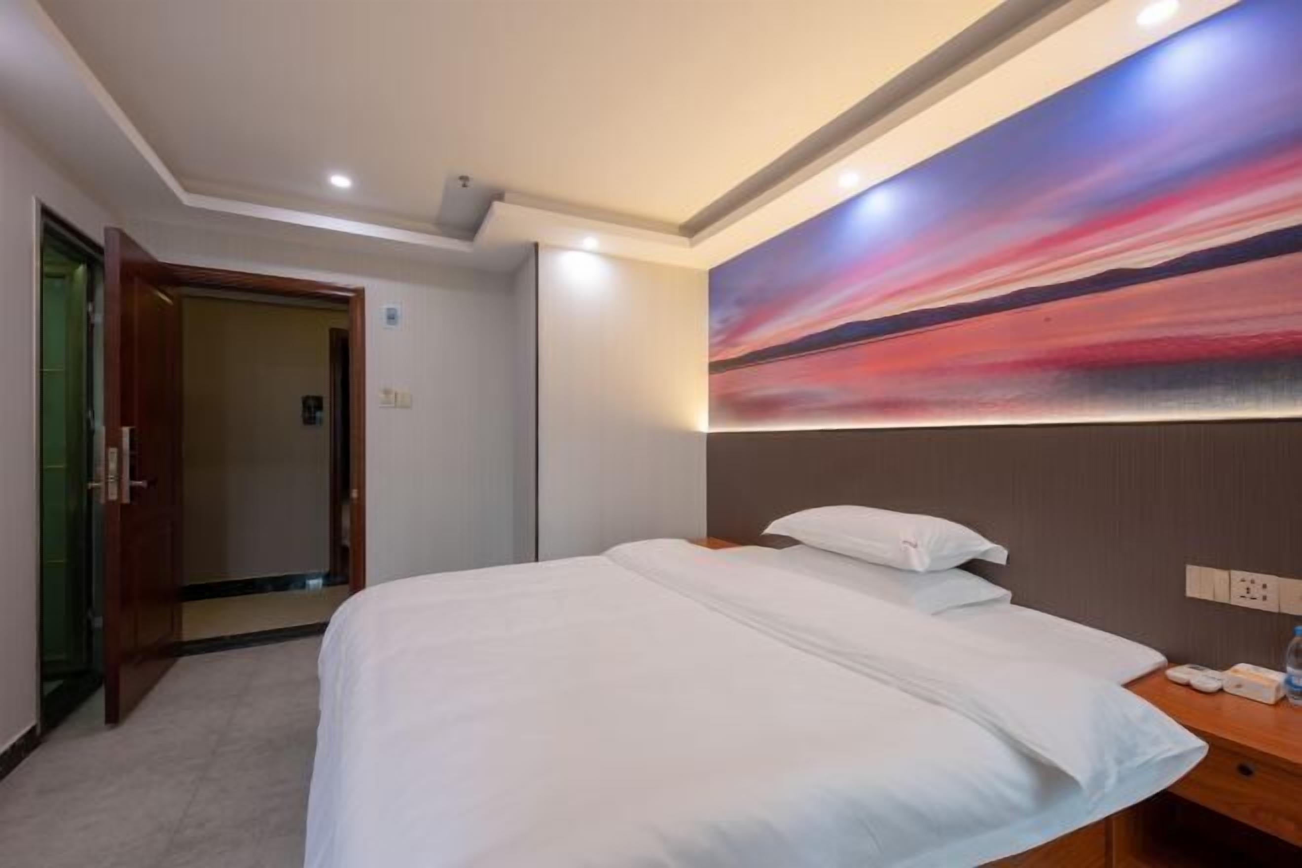 Une chambre d’hôtel avec un grand lit, une table de chevet en bois, un tableau au mur et une porte donnant sur une autre pièce.