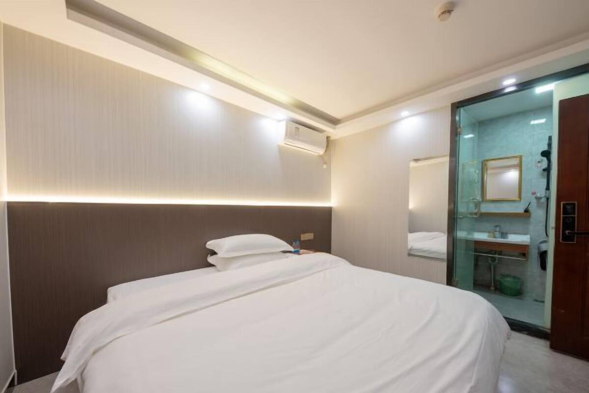 A hotel room with a bed, a glass shower enclosure, and a wall-mounted air conditioning unit.