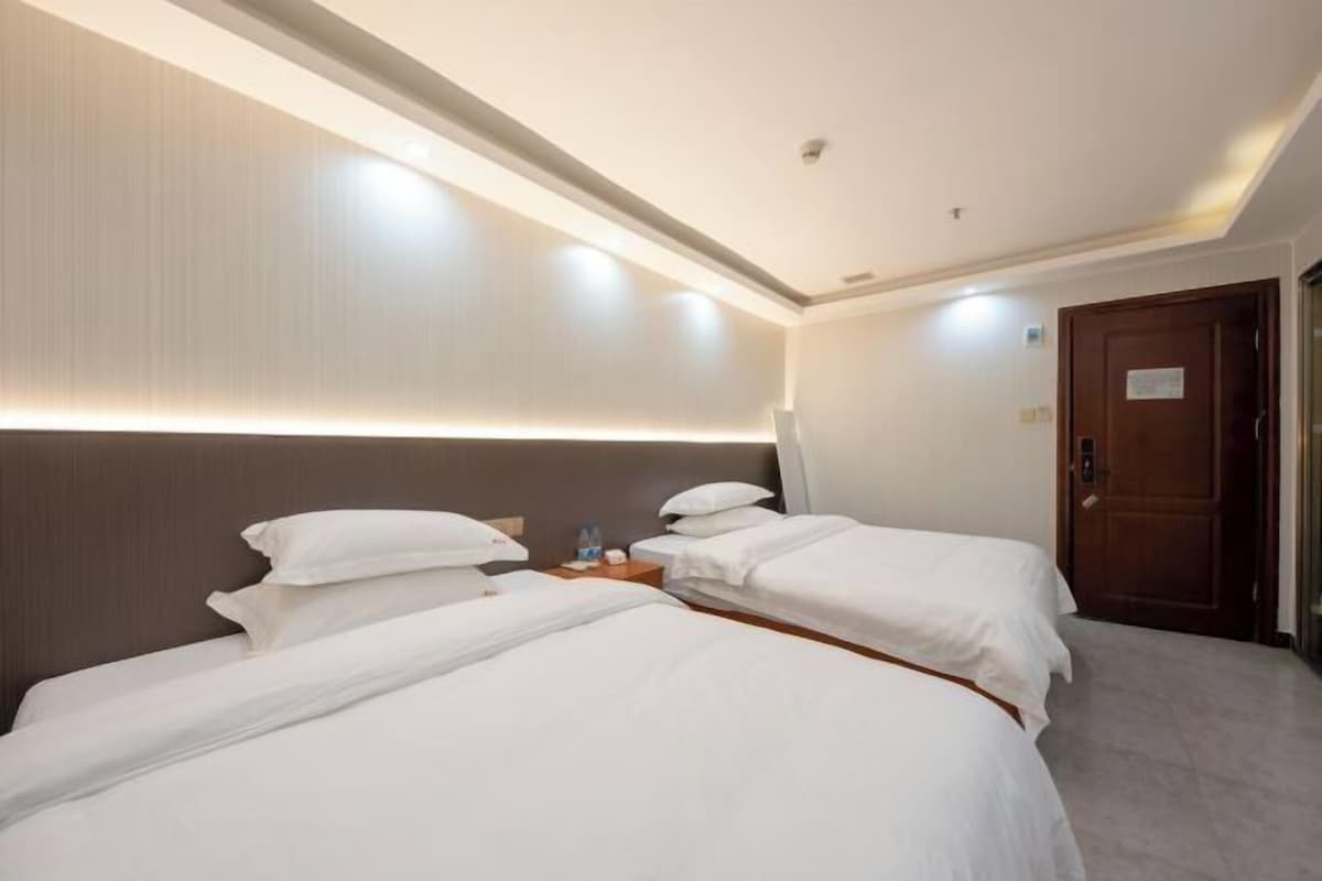 A hotel room with two single beds, a wooden headboard, a nightstand with a lamp, and a door with a sign.