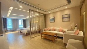 A modern hotel room with a large bed, a sofa, a coffee table, and a sliding glass door leading to a balcony. - Qinheyuan Linxuan Holiday Hotel (Haining)