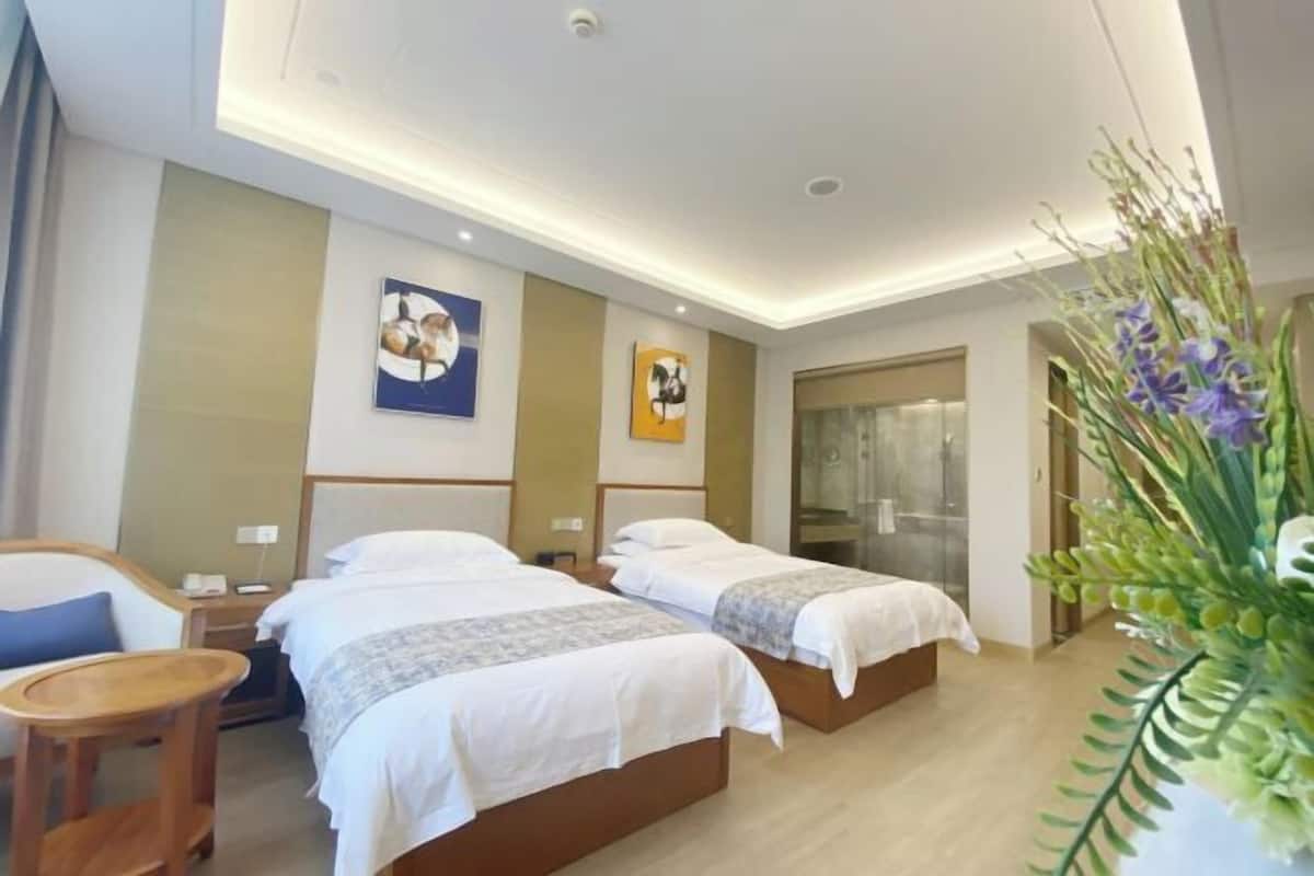A hotel room with two beds, a small table, a chair, and a large mirror.