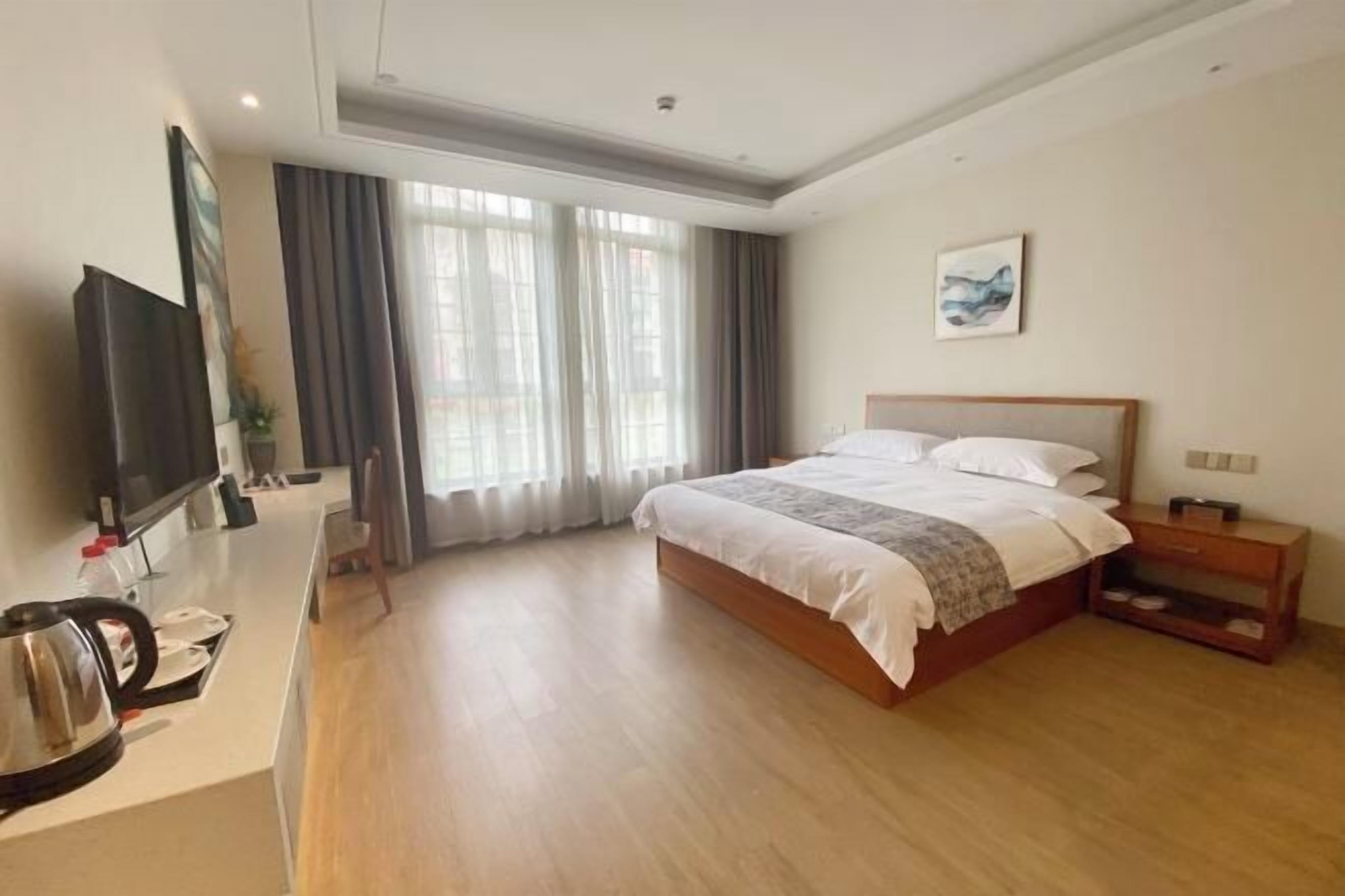 Une chambre d’hôtel avec un grand lit, un téléviseur posé sur un bureau et une fenêtre avec des rideaux.