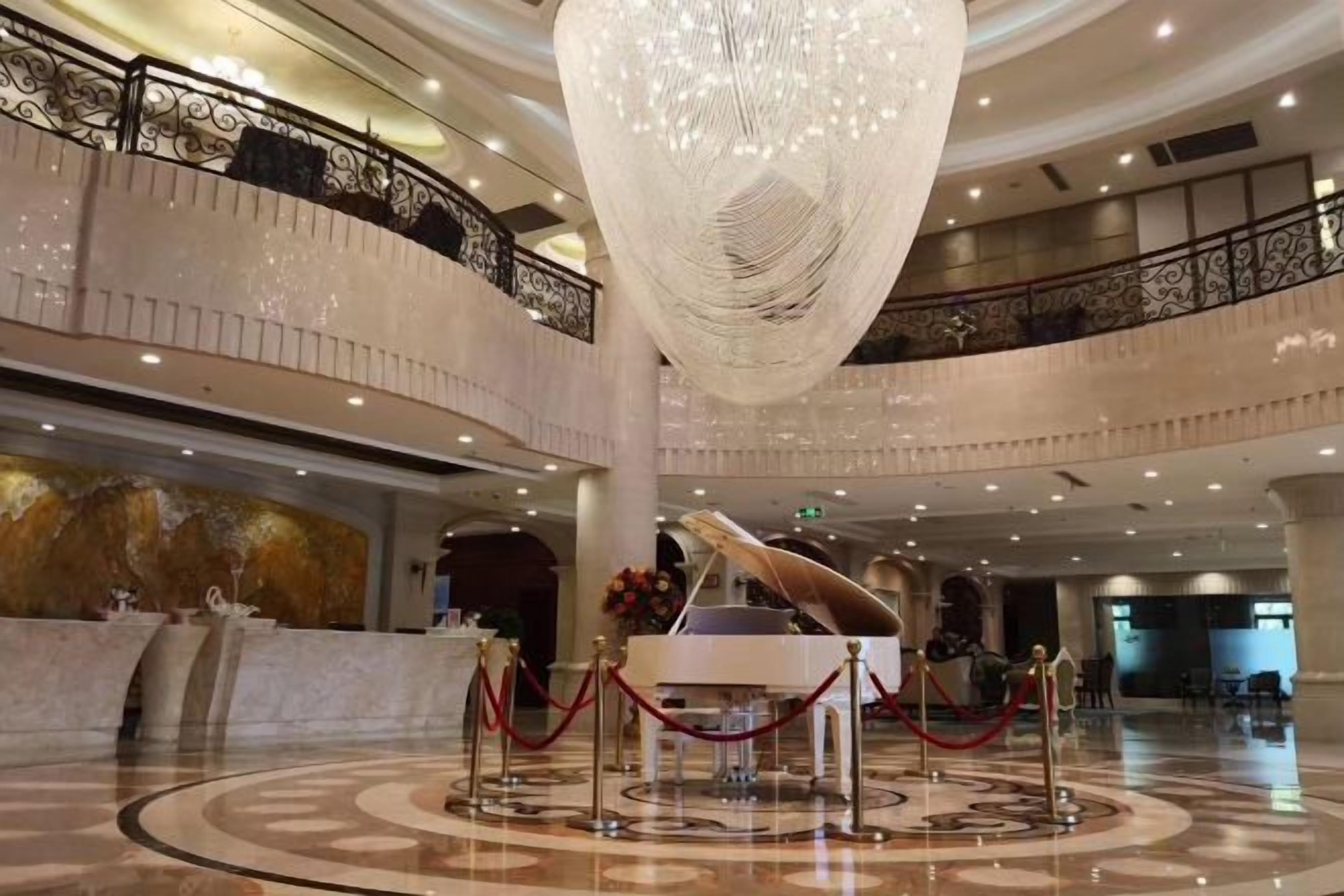 A grand lobby with a large chandelier, a grand piano, and a reception desk.