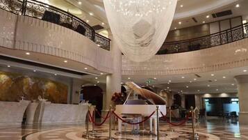 A grand lobby with a large chandelier, a grand piano, and a reception desk.