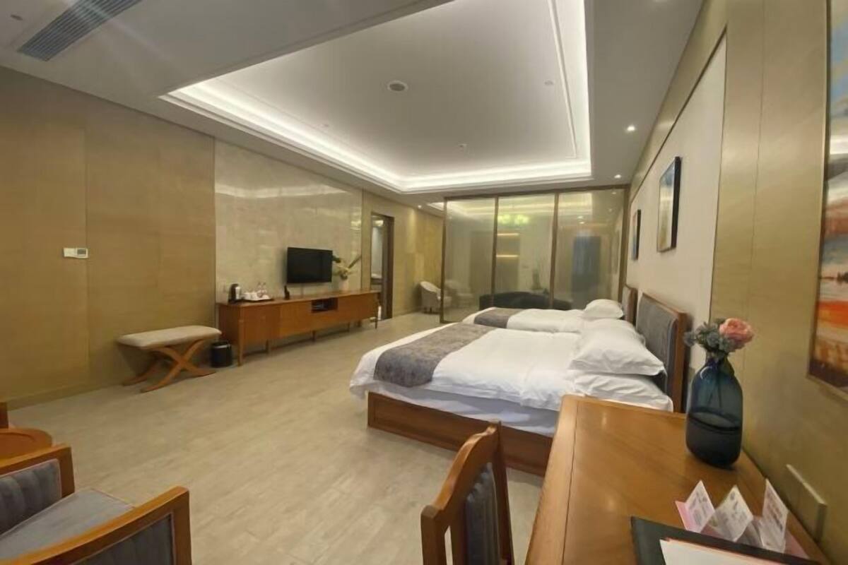 A hotel room with a bed, a desk, a chair, a TV, and a bathroom with a mirror and shower.