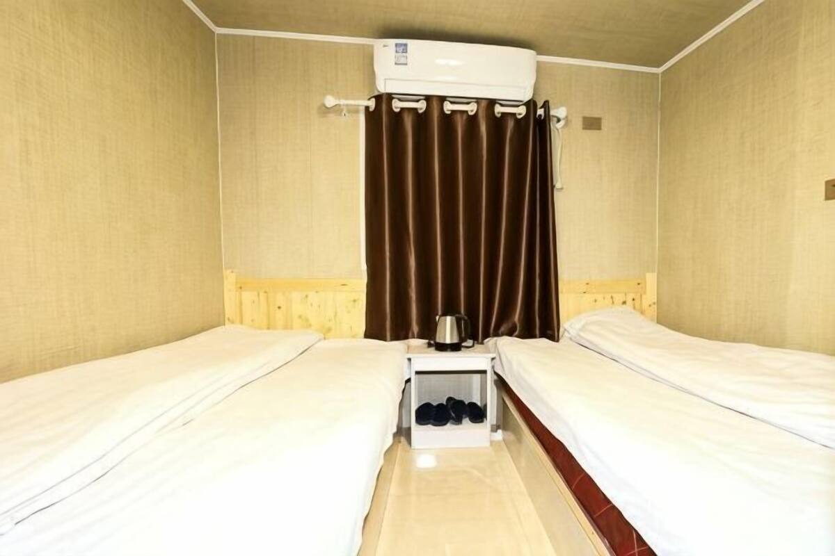 Une chambre avec deux lits, une petite table et une bouilloire, ainsi qu’un appareil de climatisation installé au plafond.