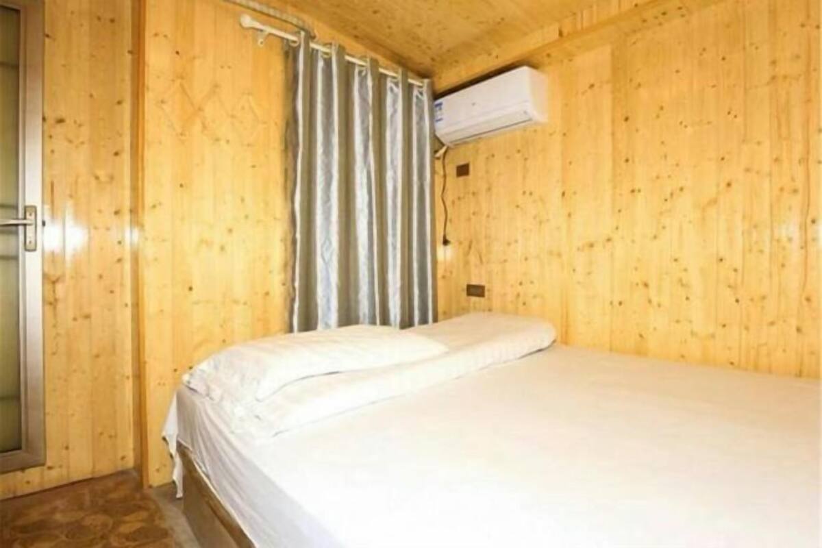 Un lit simple dans une pièce en bois, avec un rideau, un appareil de climatisation et une porte.