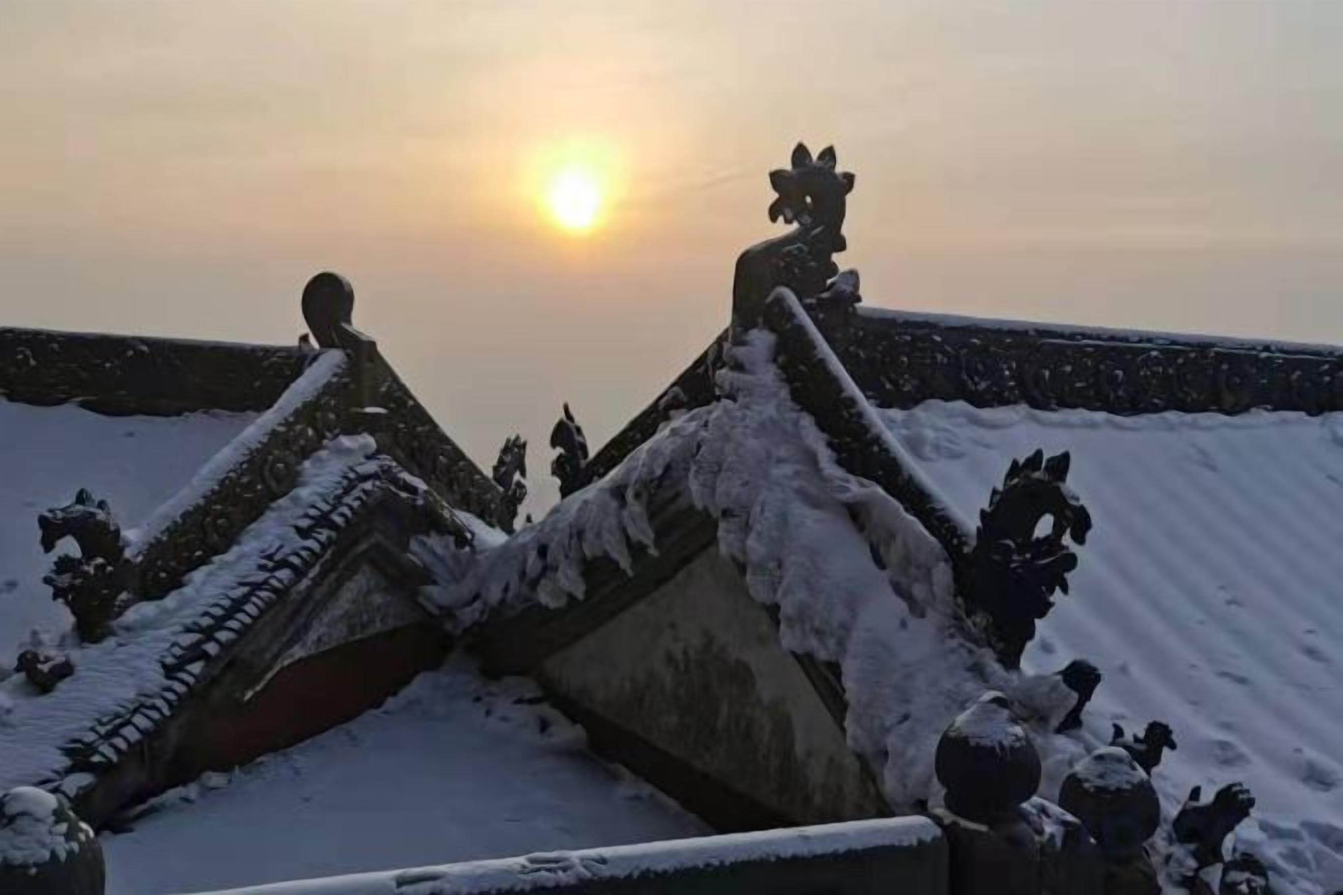 A snow-covered roof with traditional architectural elements, a clear sky, and the sun setting in the background.