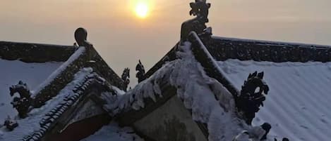 A snow-covered roof with traditional architectural elements, a clear sky, and the sun setting in the background.