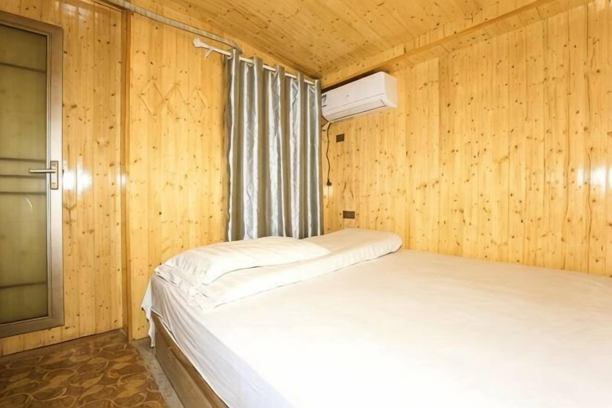 Une pièce aux murs lambrissés, comprenant un lit, une porte et un appareil de climatisation.