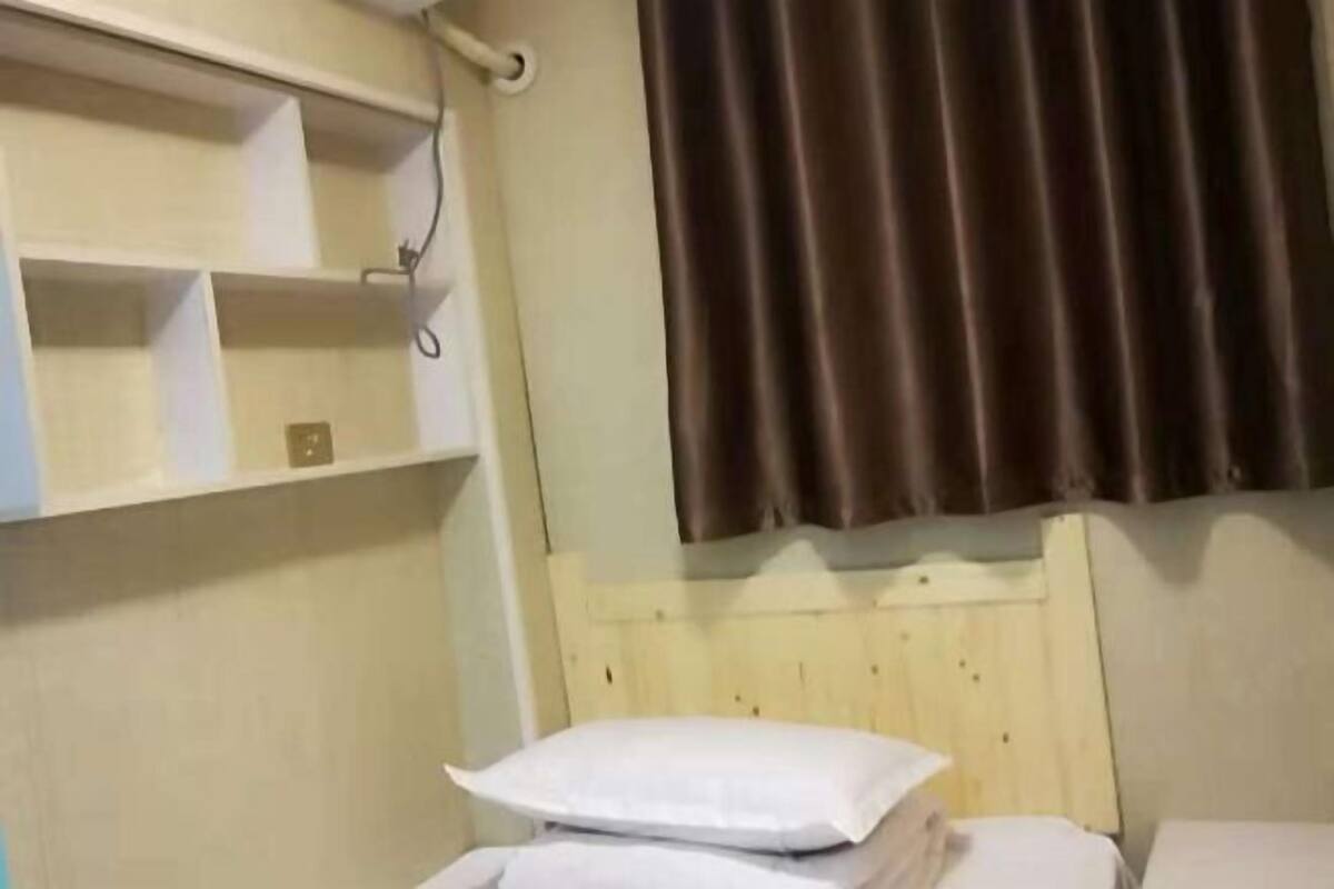 Une chambre d’hôtel avec une tête de lit en bois, un lit avec une literie blanche, une étagère avec quelques objets et un rideau marron.