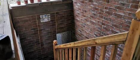 A narrow stairway with a wooden handrail, a brick wall, and potted plants on the landing.