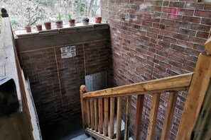 A narrow stairway with a wooden handrail, a brick wall, and potted plants on the landing.