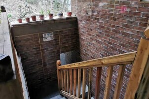 A narrow stairway with a wooden handrail, a brick wall, and potted plants on the landing.