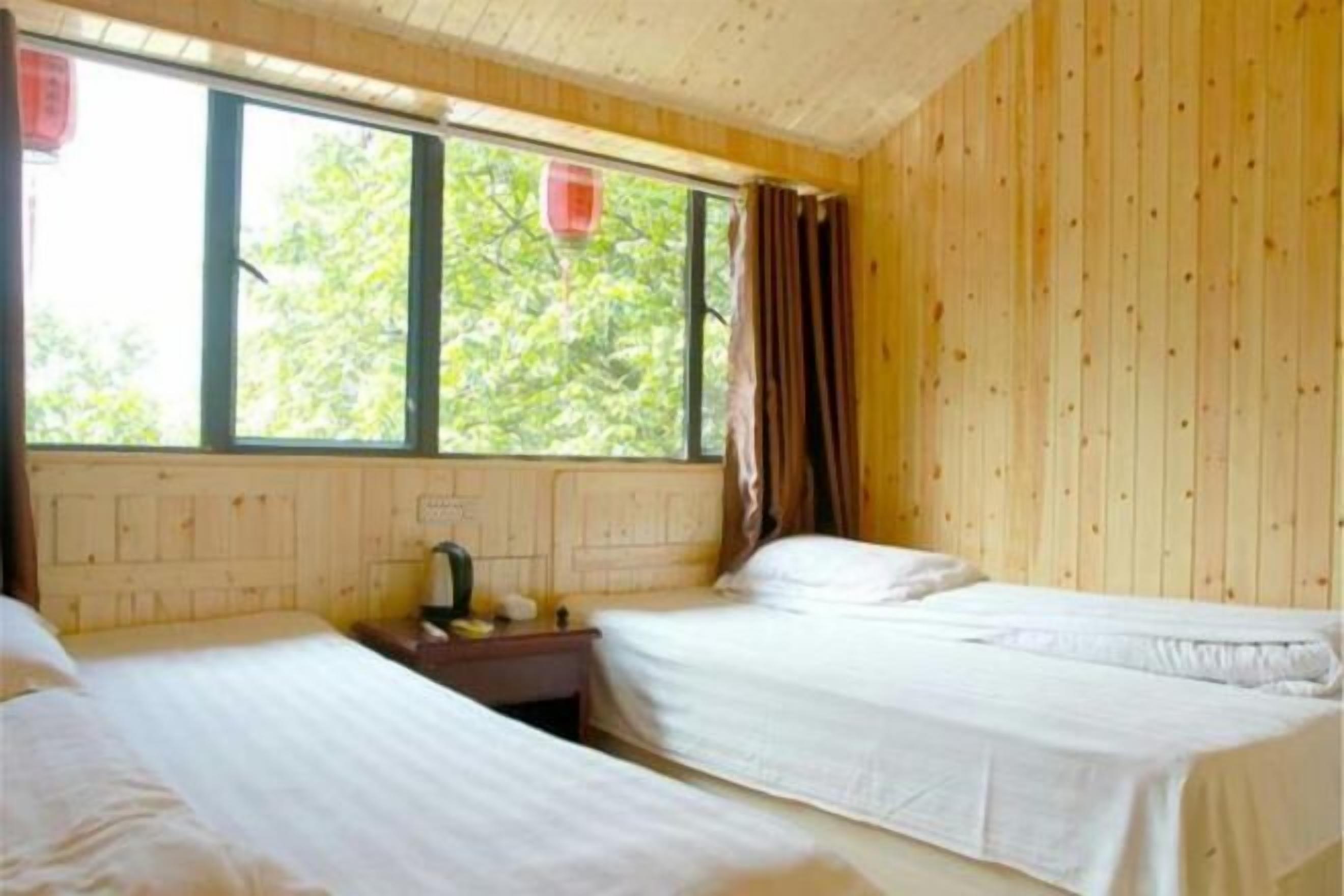 Una habitación con dos camas, cabecero de madera, una ventana con cortinas y una mesita de noche con lámpara.