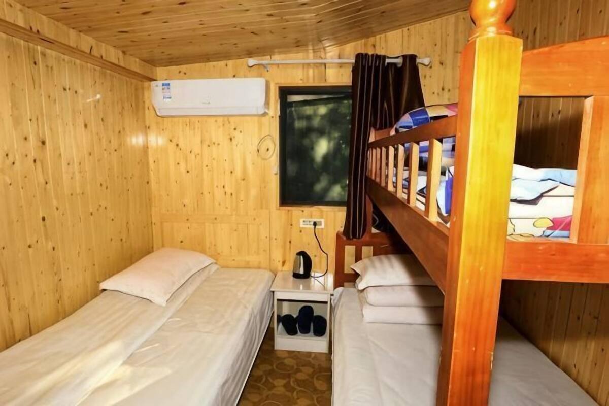 Une cabane en bois avec deux lits simples, une petite table avec une bouilloire et une fenêtre avec des rideaux.