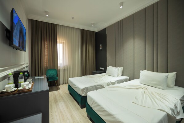 Habitación de hotel con dos camas, televisor, escritorio con cafetera y una silla.