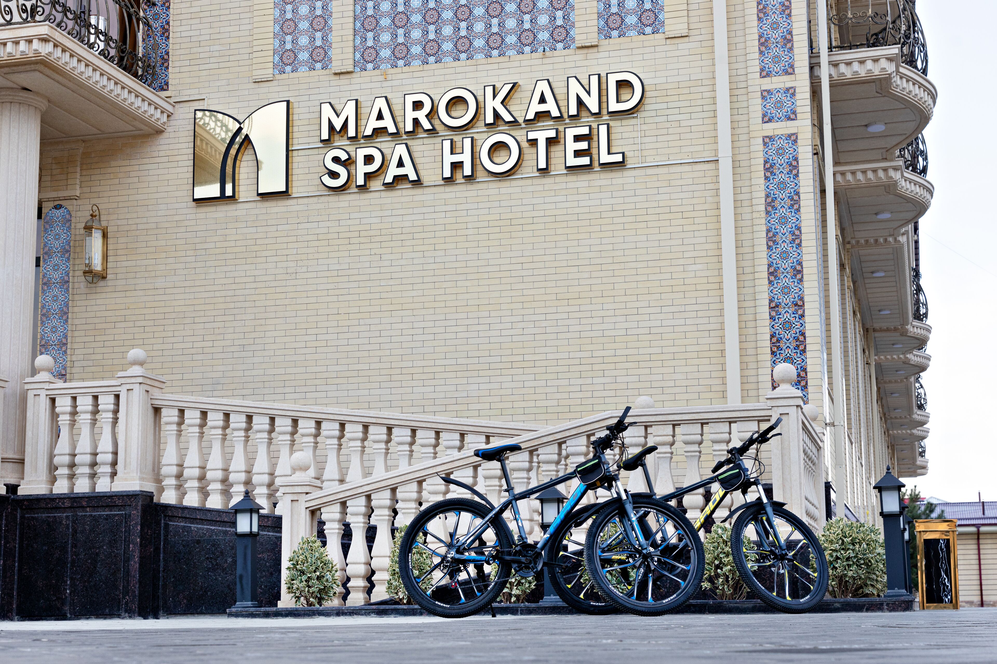 Exterior del hotel spa Marokand, con un cartel, una entrada vigilada y dos bicicletas estacionadas al frente.