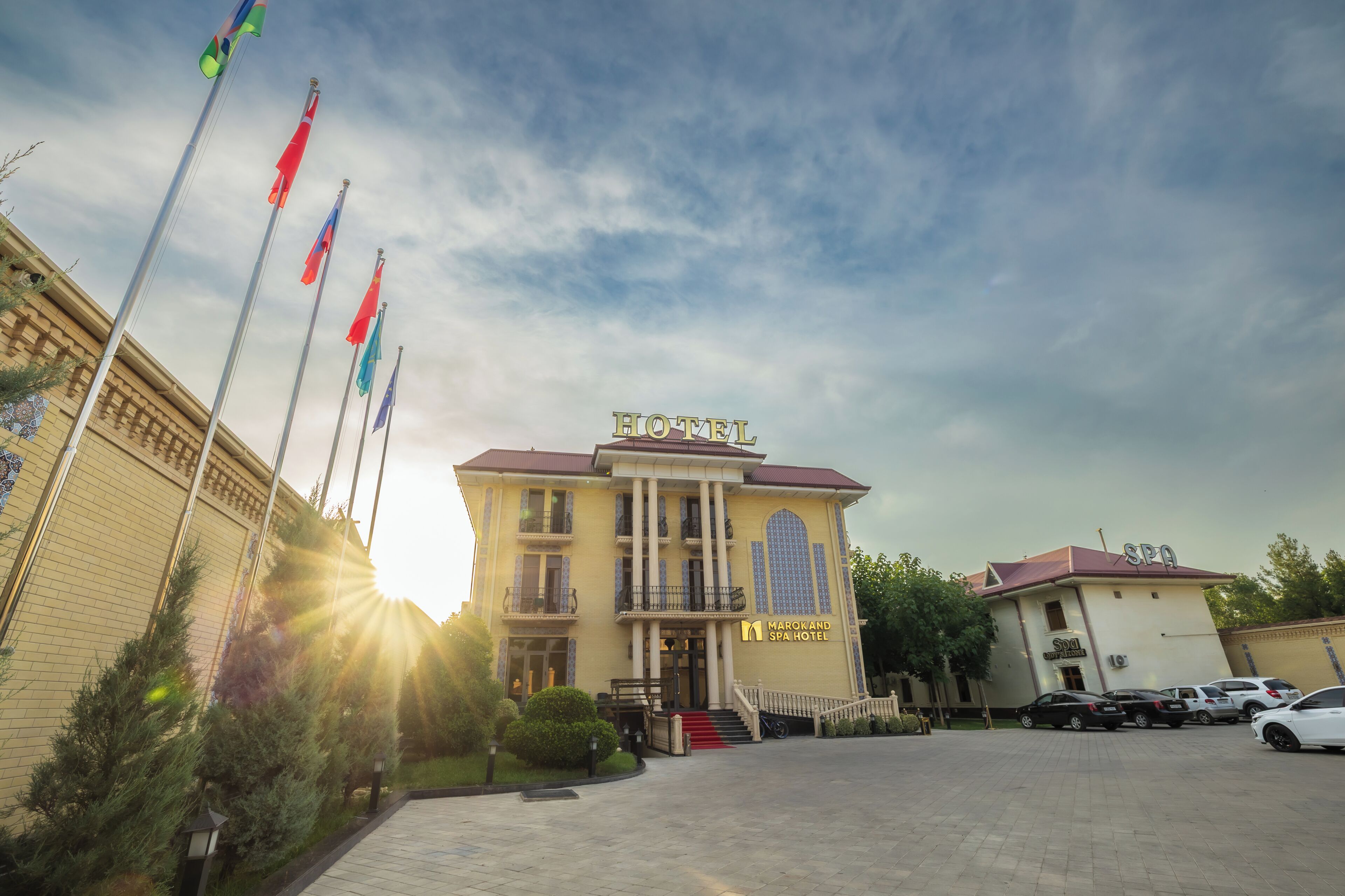 A hotel with a central entrance, multiple flags, and a parking area.