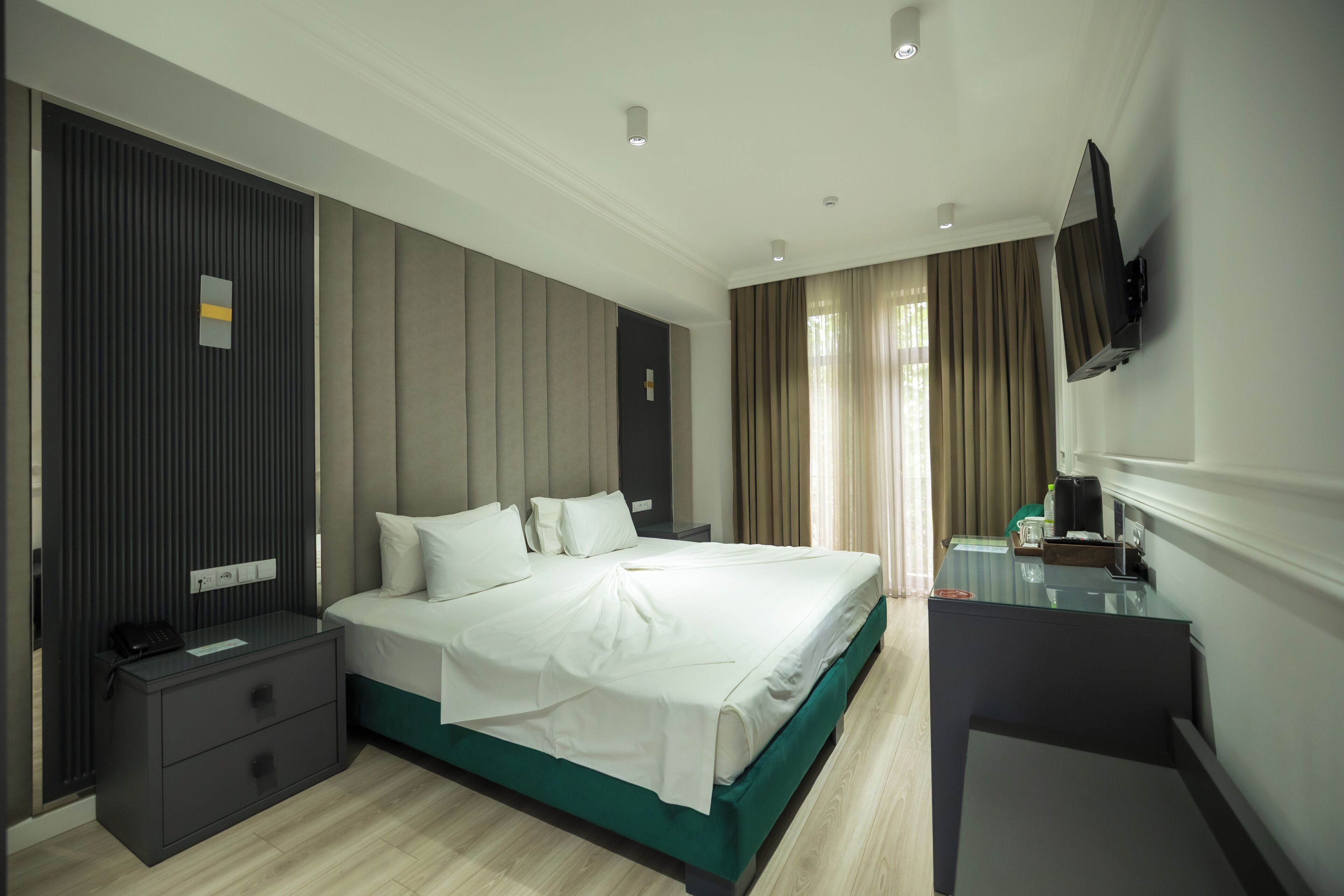 A modern hotel room with a large bed, a desk, a flat-screen TV, and a nightstand.