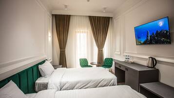 A hotel room with two beds, a desk, a chair, a television, and a view of the sea.
