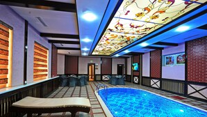 Zona de piscina con suelo de baldosas, sillas de descanso y techo con lámpara decorativa.
