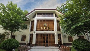 Un edificio de spa con una amplia entrada, dos bancos y un paseo cubierto de baldosas.