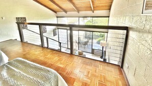 Una habitación amplia con techo de madera, vistas a través de ventanas grandes y un balcón con mobiliario exterior.