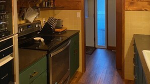 Una cocina con paredes de madera, horno empotrado, estufa y lámpara colgante.