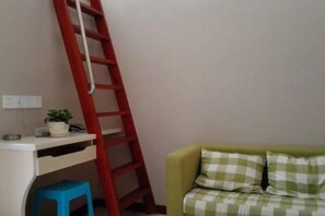 A room with a white desk, a red ladder leaning against the wall, a blue stool, and a green sofa with checkered cushions. - Buding Inn (Yi County)