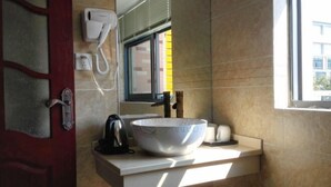 A bathroom with a white sink, a large mirror, a white electric heater, and a window with a view of buildings. - Buding Inn (Yi County)