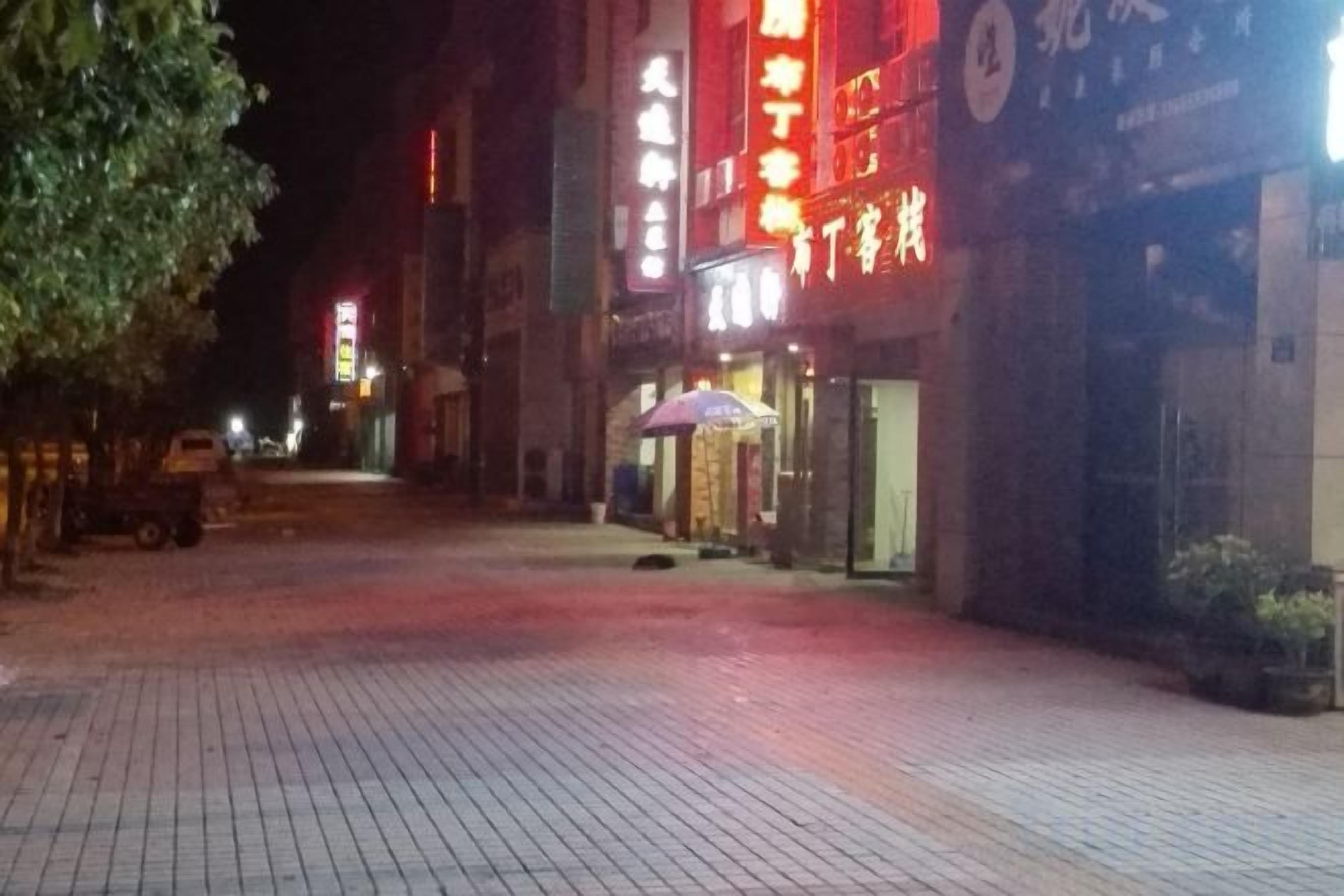 A nighttime street scene with illuminated storefronts and a paved walkway.