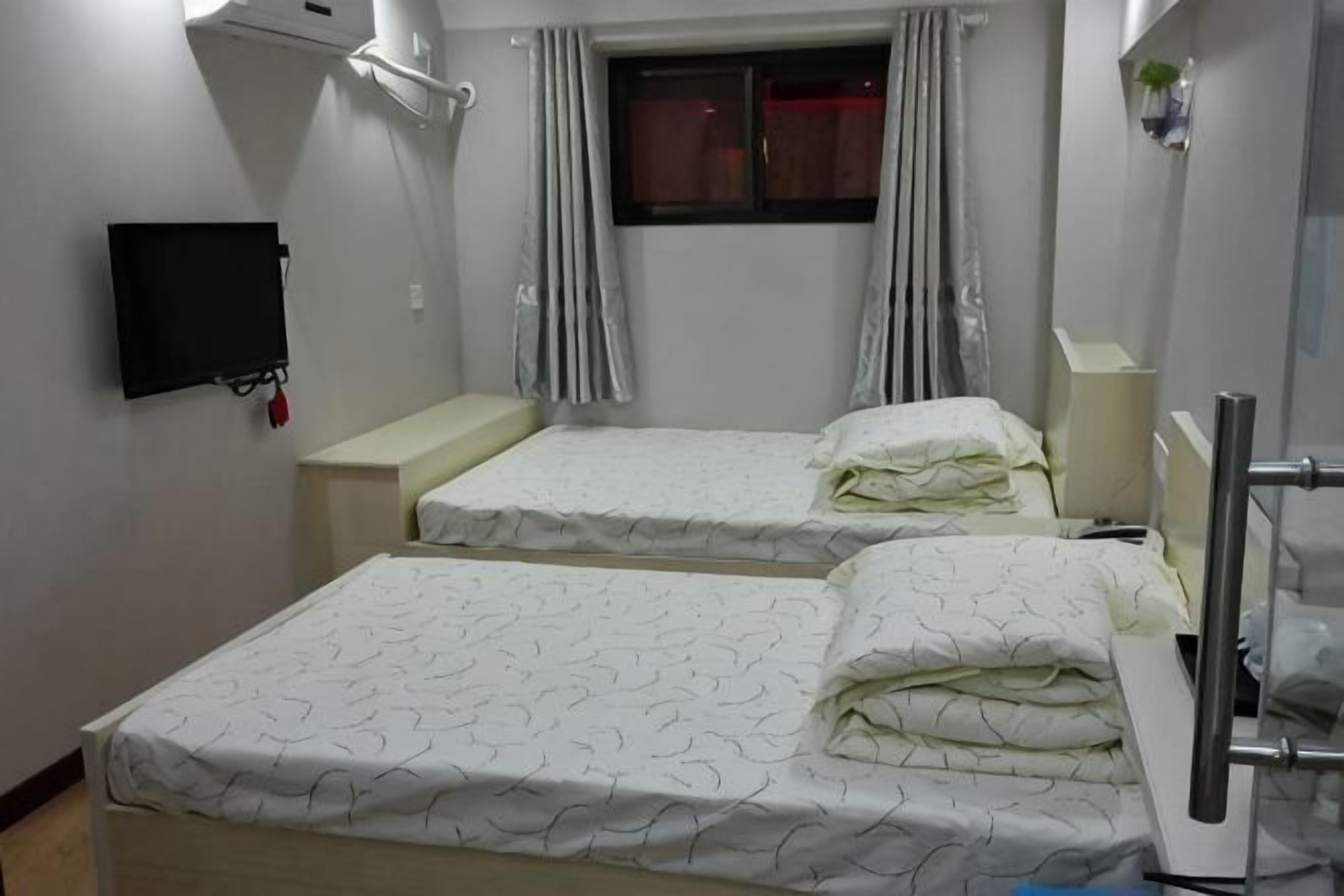 A hotel room with two beds, a TV, a window with curtains, and a bedside table.