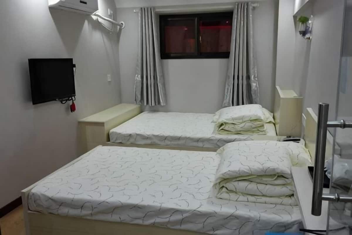 A hotel room with two beds, a TV, a window with curtains, and a bedside table.