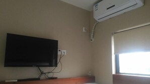 A hotel room with a flat-screen TV mounted on the wall, an air conditioning unit above it, and a window with a blind. - Buding Inn (Yi County)