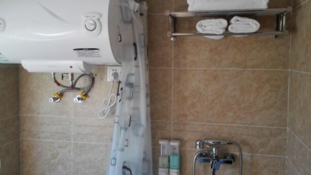 A bathroom with a shower, a towel rack with towels, a toilet, and a hand dryer. - Buding Inn (Yi County)